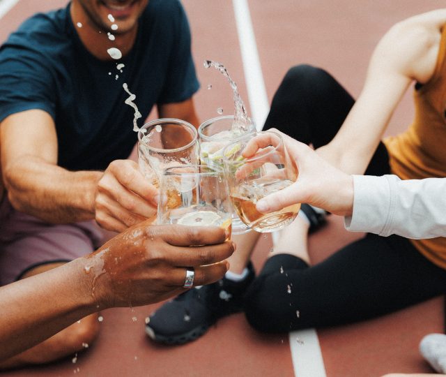 four people siting on the ground clinking govino unbreakable glasses fairly hard that their drinks come out the top