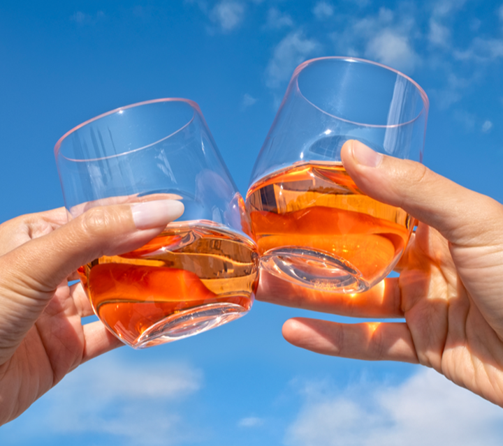 zoom in of two hands clinking govino glasses with blue sky background